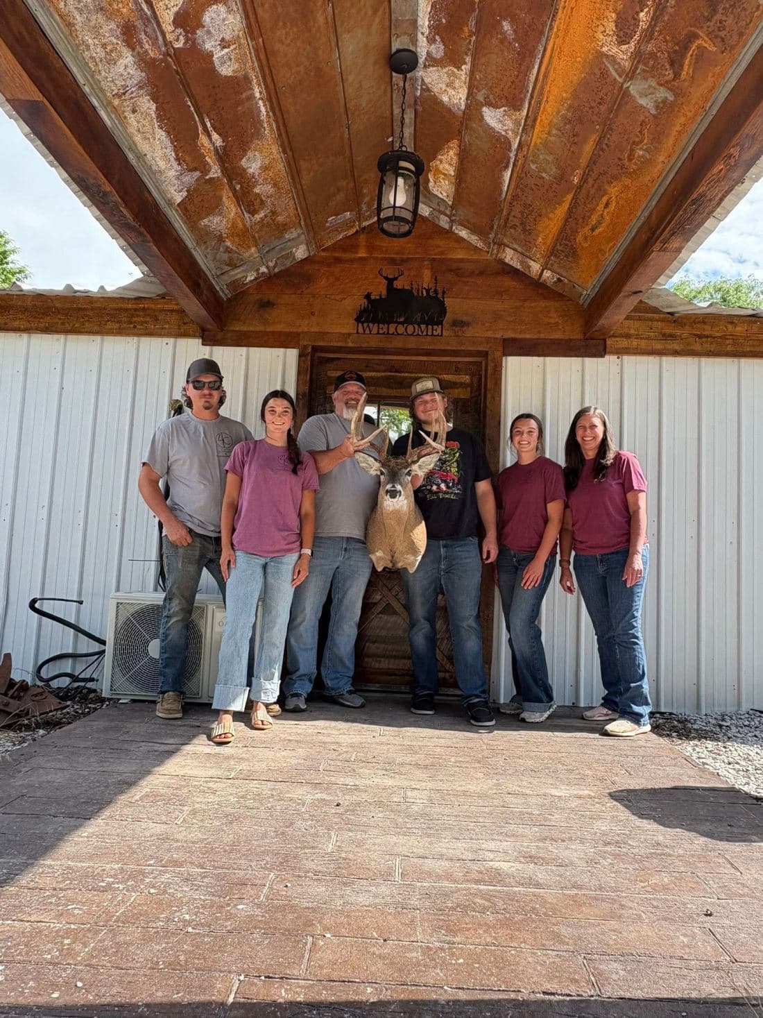 The 4C crew standing under the shop's covered entry with a whitetail mount